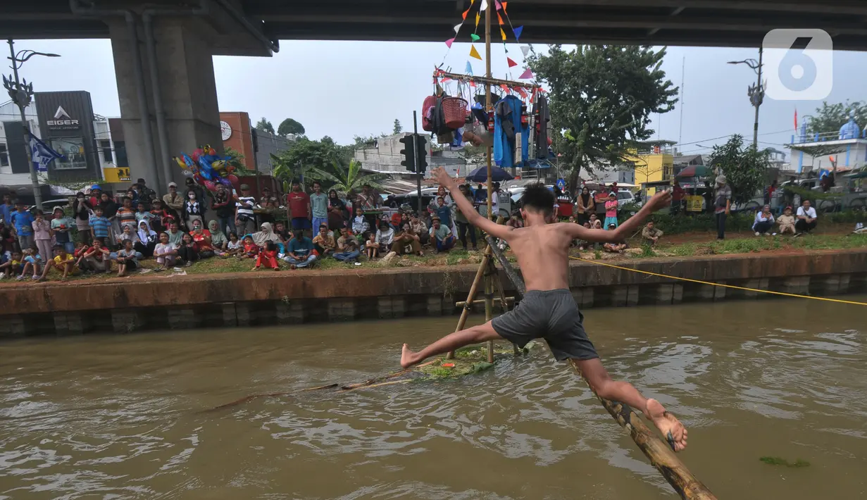 Warga Kalimalang mencoba melewati bambu yang telang dilumuri oli untuk mencapai pinang dalam lomba Titian Bambu di RW 04, Kelurahan Cipinang Melayu, Kecamatan Makasar, Jakarta Timur, Sabtu (24/8/2024). (merdeka.com/Imam Buhori)