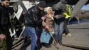Relawan melewati jalan setapak di bawah jembatan yang hancur saat mereka mengevakuasi seorang warga lanjut usia di Irpin, barat laut Kiev, pada Jumat (11/3/2022). Invasi Rusia ke Ukraina sudah memasuki hari ke-16 pada hari Jumat ini. (AP Photo/Efrem Lukatsky)