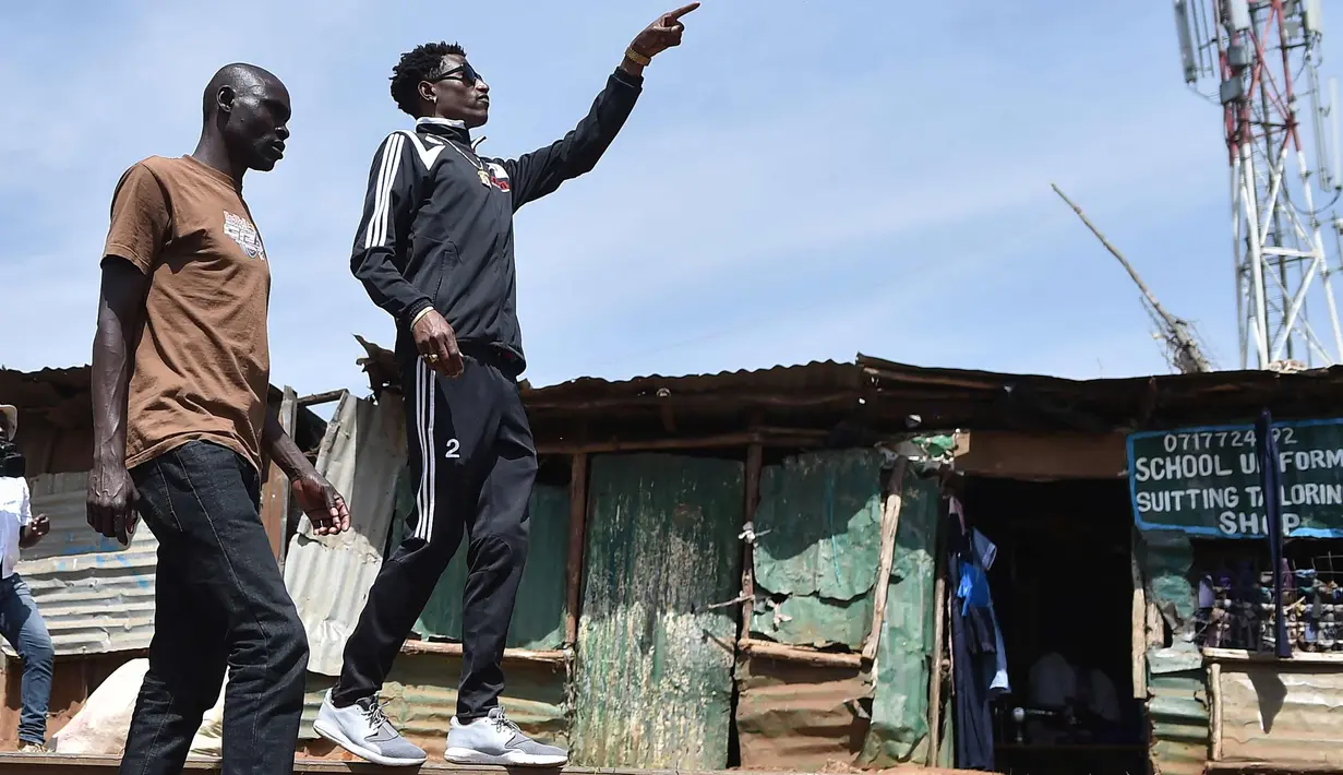 Artis hip hop Kenya Henry Ohanga berjalan dengan temannya di sepanjang jalur kereta api saat di Kibera di Nairobi, Kenya (16/1). Octopizzo 29 tahun saat ini menjadi salah satu bintang hip-hop paling terkenal di Afrika Timur. (AFP Photo/Tony Karumba)