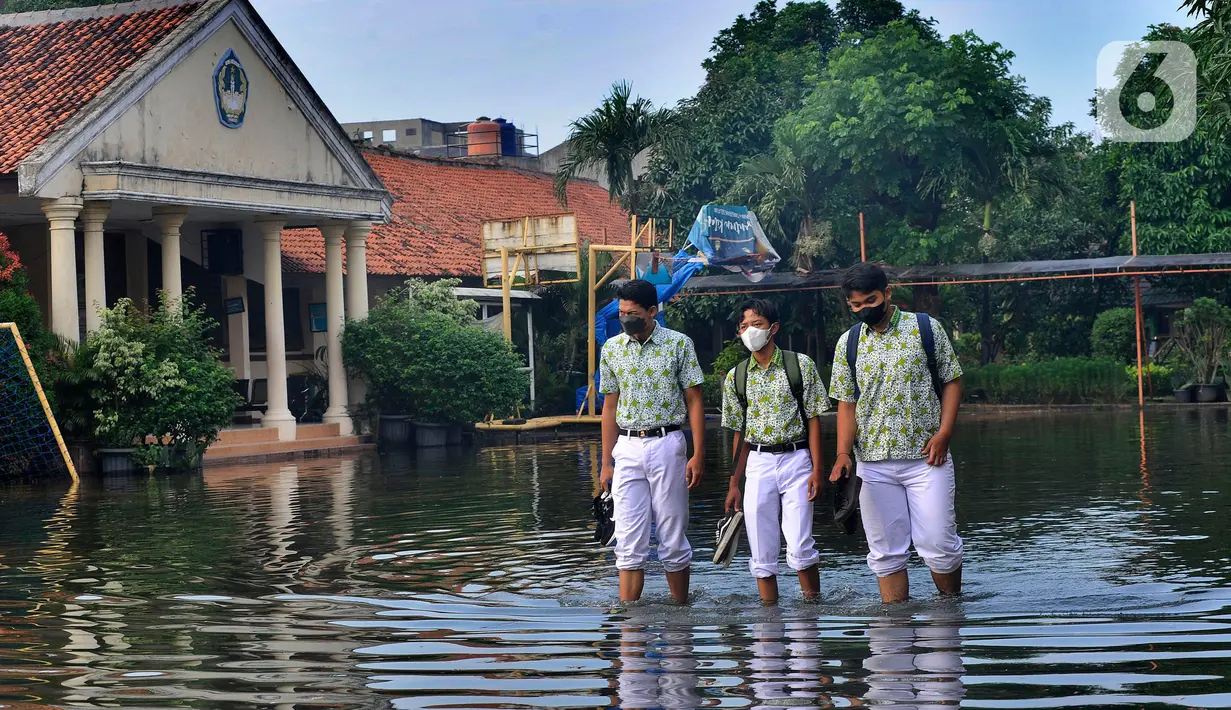 Siswa berjalan melewati banjir yang menggenangi halaman  sekolah di SMAN 4 Tangsel, Pondok Ranji, Tangerang Selatan, Banten, Selasa (14/6/2022). Tiga  pekan lebih banjir merendam lapangan sekolah itu dikarenakan tertutupnya saluran air oleh sampah yang berasal dari tempat pembuangan sampah (TPS) ilegal. (merdeka.com/Arie Basuki)