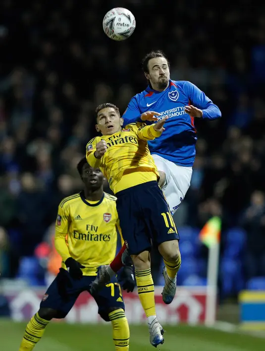 Pemain Portsmouth, Ryan Williams (kanan) melompat saat berebut bola dengan gelandang Arsenal, Lucas Torreira pada laga putaran lima Piala FA di Fratton Park, Senin (2/3/2020). Arsenal sukses membungkam tuan rumah Portsmouth dengan skor 2-0. (Adrian DENNIS/AFP)