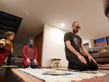 Ahmad Kamel (depan) melaksanakan salat Maghrib dengan istrinya, Nadia Chaouch, ketika putra mereka Ahmad Kamel berlari melewati setelah keluarga berbuka puasa saat bulan Ramadan selama wabah Covid-19 di rumah mereka di Seattle (28/4/2020). (AP/Elaine Thompson)