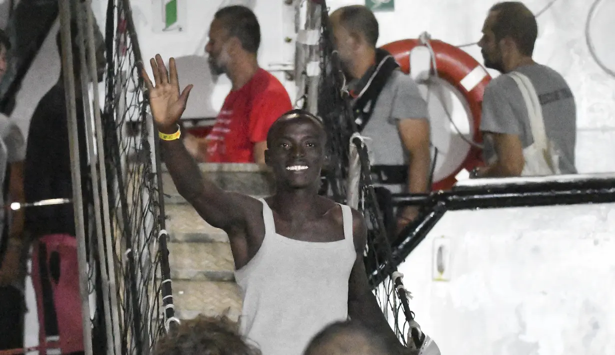 Seorang pria melambai sambil tersenyum ketika turun dari kapal penyelamat Open Arms di pulau Sisilia Lampedusa, Italia (20/8/2019). Sebelumnya permintaan untuk berlabuh di Italia ditolak, kapal Open Arms yang membawa imigran Afrika akhirnya diizinkan. (AP Photo/Salvatore Cavalli)