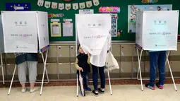 Seorang anak mengintip dari bilik suara saat ibunya menggunakan hak suara untuk memilih presiden baru di sebuah TPS di Seoul, Selasa (9/5). Hari ini, warga Korsel mulai untuk memilih presiden baru setelah pemakzulan Park Geun-hye. (AP Photo/Lee Jin-man)