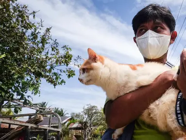 Seorang relawan menyelamatkan kucing dari sebuah rumah yang ditinggalkan saat penduduk dievakuasi setelah letusan gunung berapi Gunung Ruang di Pulau Tagulandang di Sitaro, Sulawesi Utara pada tanggal 4 Mei 2024. (Ronny Adolof BUOL/AFP)