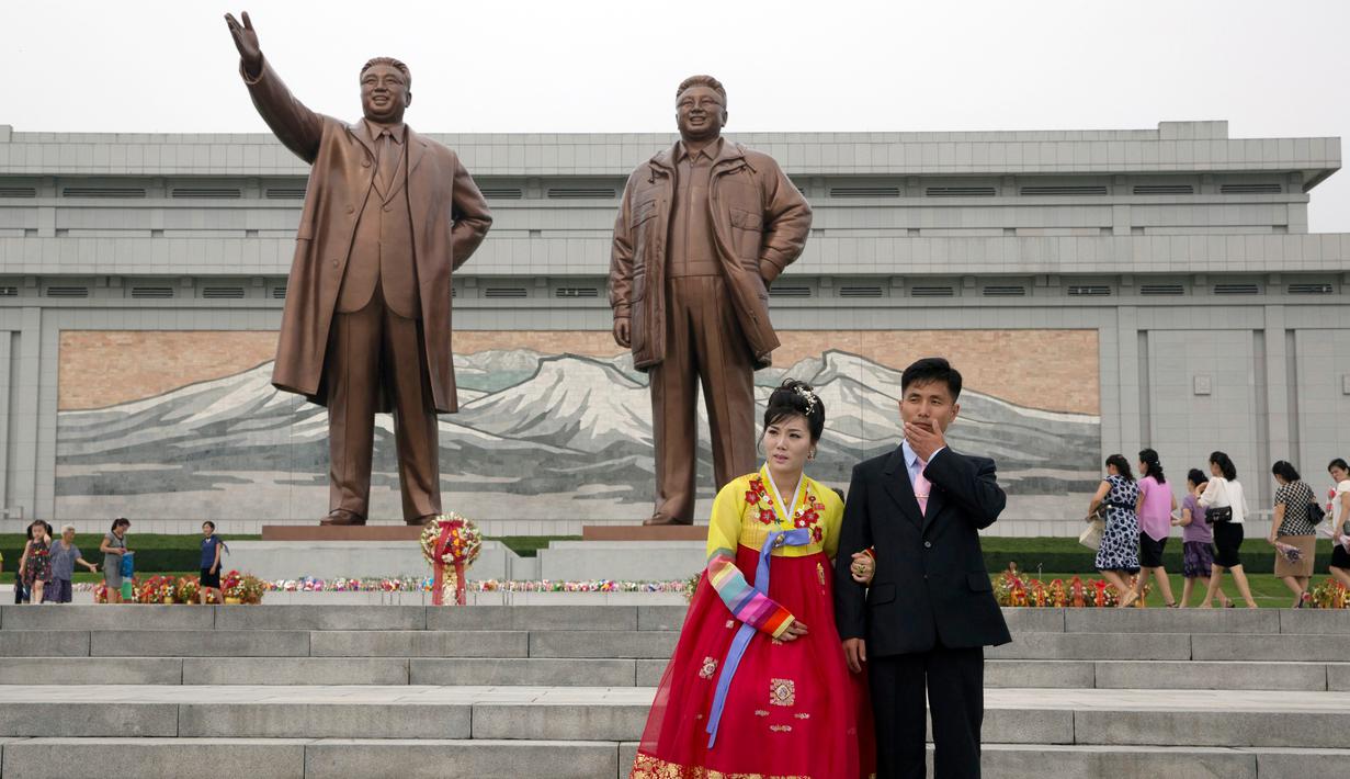 Pasangan pengantin berdiri di dekat patung perunggu raksasa pemimpin Korea Utara Kim Il Sung dan Kim Jong Il dalam peringatan berakhirnya Perang Dunia II dan pembebasan dari kolonial Jepang di Pyongyang, Korut, Rabu (15/8). (AP Photo/Ng Han Guan)