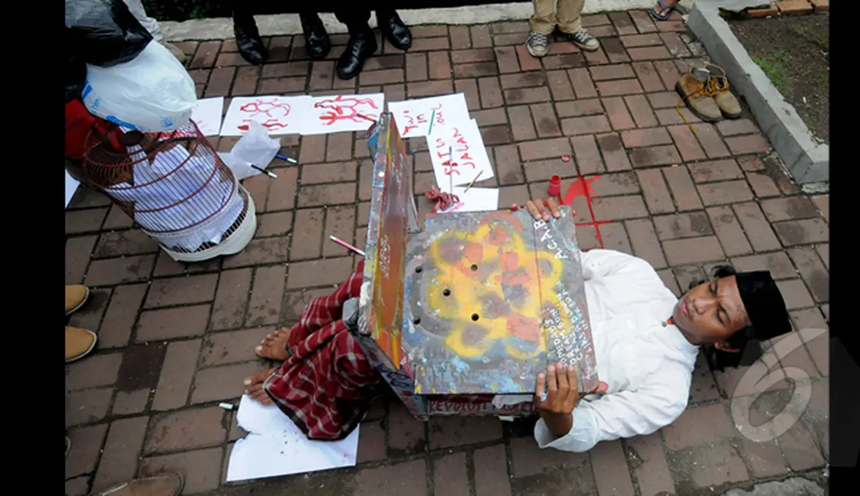 Seorang Seniman saat melakukan aksi teatrikal tidur dibawah kursi di depan Gedung Komisi Pemberantasan Korupsi (KPK), Jakarta, Senin (26/1/2014). (Liputan6.com/Herman Zakharia)