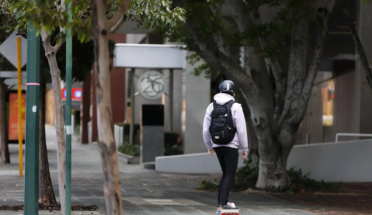 Seorang pria mengendarai skateboard listrik di sepanjang jalan setapak yang sepi di Perth (29/6/2021). Warga di Kota Perth, ibu kota Australia Barat, dan wilayah tetangga Peel harus tinggal di rumah kecuali untuk alasan mendesak. (AFP/Trevor Collens)