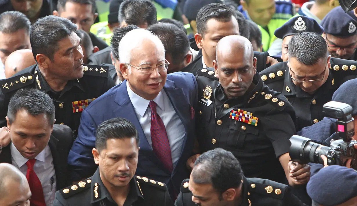 Mantan Perdana Menteri Malaysia, Najib Razak dengan pengawalan ketat tiba di Pengadilan Kuala Lumpur untuk didakwa pertama kalinya, Rabu (4/7). Najib sebelumnya telah ditangkap Komisi Anti-Korupsi Malaysia kemarin sore di kediamannya. (AP/Vincent Thian)