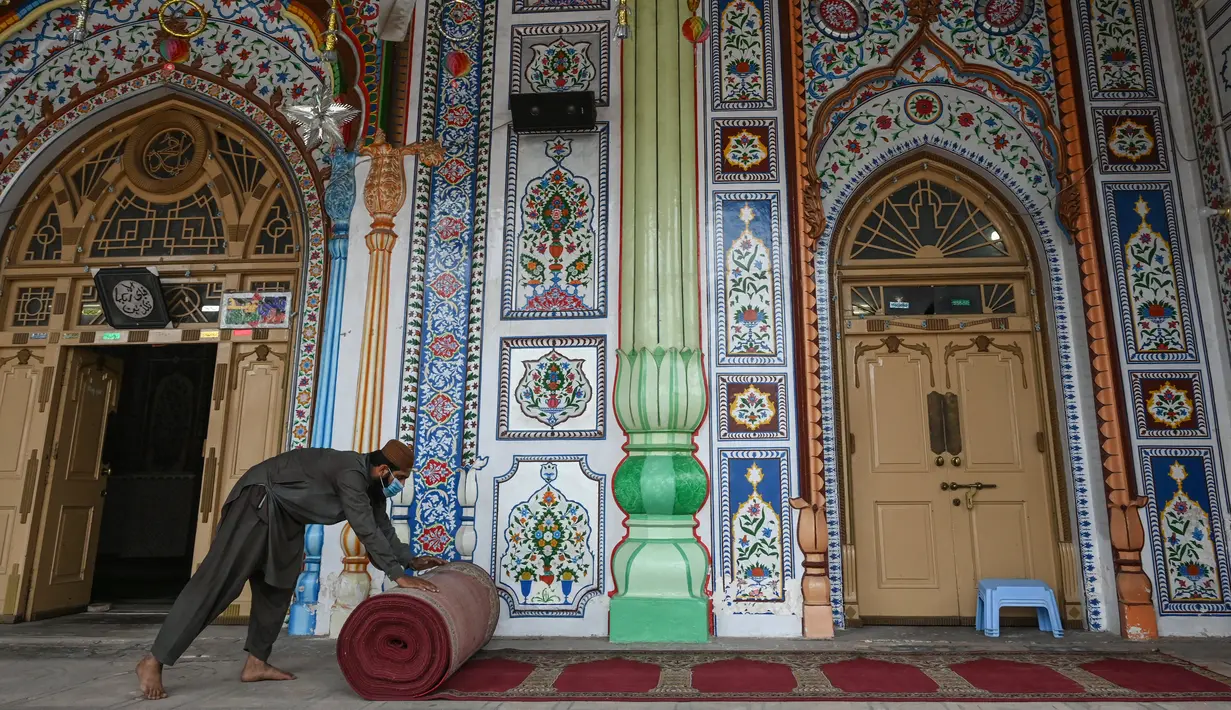 Umat Muslim menggulung karpet sajadah dari aula utama masjid menyusul pembatasan baru pemerintah baru di Rawalpindi, Senin (5/4/2021). Pejabat kesehatan Pakistan telah meminta masjid-masjid mengambil langkah-langkah khusus untuk menahan penyebaran COVID-19 selama Ramadan. (Aamir QURESHI/AFP)