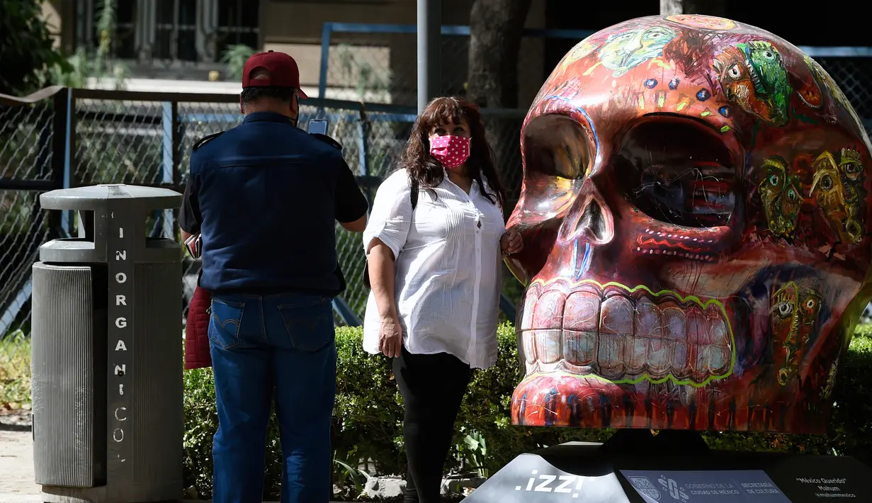 Seorang perempuan berpose dengan tengkorak yang dihias selama pameran edisi keempat "Mexicraneos" (Mexisculls) di Reforma Avenue, Mexico City pada 23 Oktober 2020. Instalasi sebanyak 55 tengkorak berbagai warna itumenghiasi jalanan sebagai bagian dari perayaan Day of the Dead. (ALFREDO ESTRELLA/AFP)