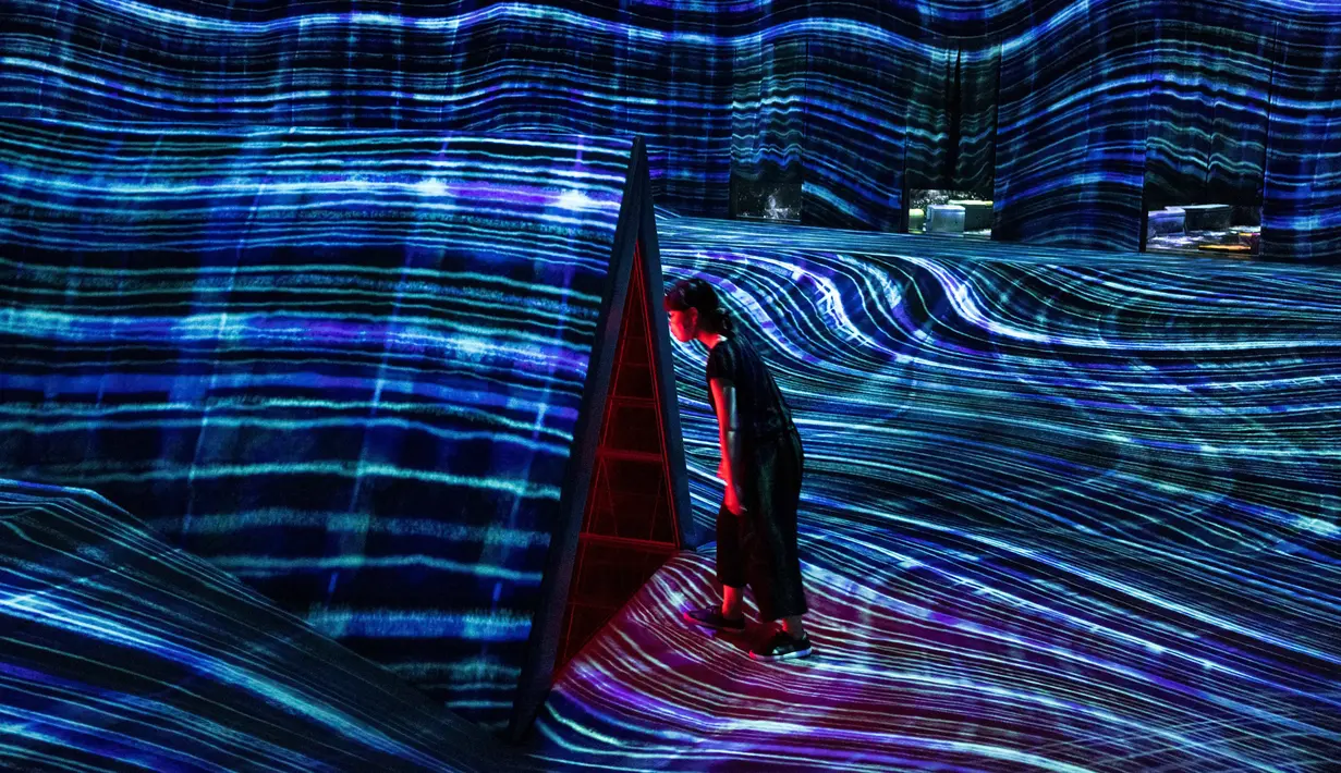 Seorang anggota staf berjalan melalui instalasi digital interaktif bernama "Beating Earth" selama pratinjau media "teamLab Forest" di gedung hiburan BOSS E・ZO FUKUOKA di Fukuoka, Jepang, Jumat (16/7/2021). (YUKI IWAMURA/AFP)