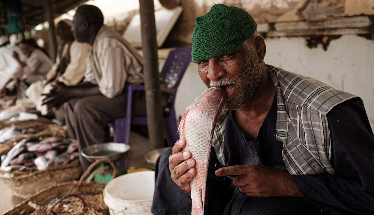 Pedagang ikan bercanda menggigit seekor ikan ketika ia difoto di sebuah pasar ikan di dekat Sungai Nil, di kota kembar Khartoum, Omdurman (24/6/2019). Omdurman merupakan kota terbesar di Sudan memiliki jumlah penduduk sebanyak 1,2 juta jiwa (1993). (AFP Photo/Yasuyoshi Chiba)