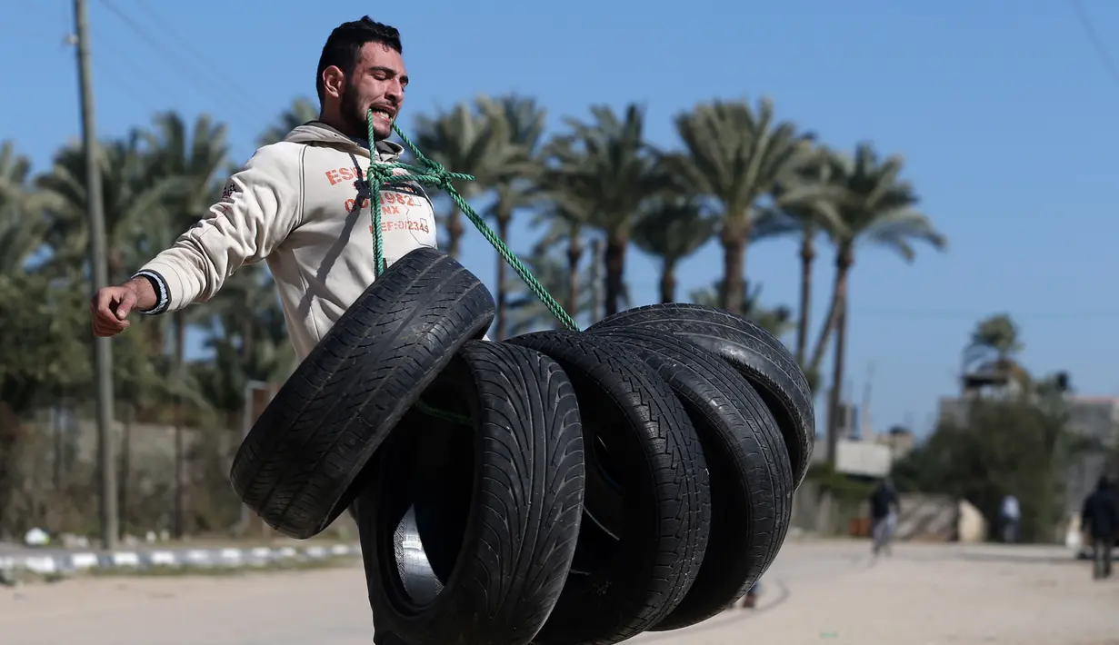 Mohamed Barka, pria yang dijuluki "Super Hero" asal Palestina saat berusaha mengangkat sejumlah ban menggunakan gigi dalam aksinya di Deir Al-Balah, Gaza Tengah, Kamis (4/2). (MOHAMMED ABED/AFP)
