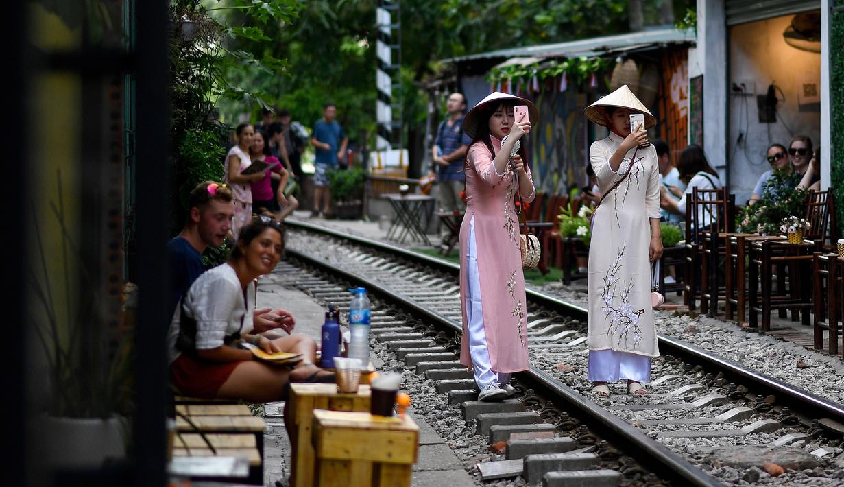 Foto pada 8 Juni 2019 menunjukkan uris mengenakan kostum tradisional Vietnam berswafoto di tengah jalur kereta api populer di Hanoi. Di ibu kota Vietnam tersebut rel-rel kereta yang berada di permukiman padat penduduk dijadikan destinasi wisata selfie. (Photo by Manan VATSYAYANA / AFP)