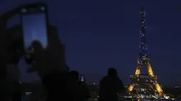 Warga memotret Menara Eiffel yang diterangi warna bendera Ukraina di Paris (25/2/2022). Pasukan Rusia menyerang ibu kota Ukraina pada Jumat (25/2) dengan tembakan dan ledakan dalam invasi ke negara demokratis yang memicu kekhawatiran perang yang lebih luas di Eropa. (AP Photo/Adrienne Surprenant)