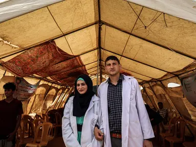 Pasangan petugas medis Muadh Al-Raqab (kanan) dan Hadeel Al-Najjar yang baru menikah berfoto di luar tenda di jalur Gaza selatan, Palestina (2/5). Petugas medis ini harus melangsungkan pernikahannya di dalam tenda. (AFP Photo/Said Khatib)