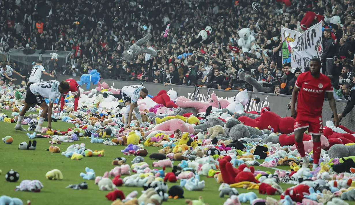 Pemain Besiktas dan Antalyaspor dibantu petugas mengumpulkan boneka yang dilemparkan oleh penonton pada laga lanjutan Liga Turki 2022/2023 yang berlangsung di Stadion Vodafone, Istanbul, Minggu (27/02/2023). Aksi tersebut ditujukan sebagai bentuk sumbangan untuk anak-anak korban gempa Turki. (AP Photo)