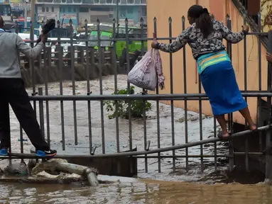 Pejalan kaki berjalan di pagar untuk menyebrang menyusuri jalan yang banjir menuju tempat kerja setelah hujan deras di Nairobi, Kenya (15/3). (AFP Photo/Simon Maina)