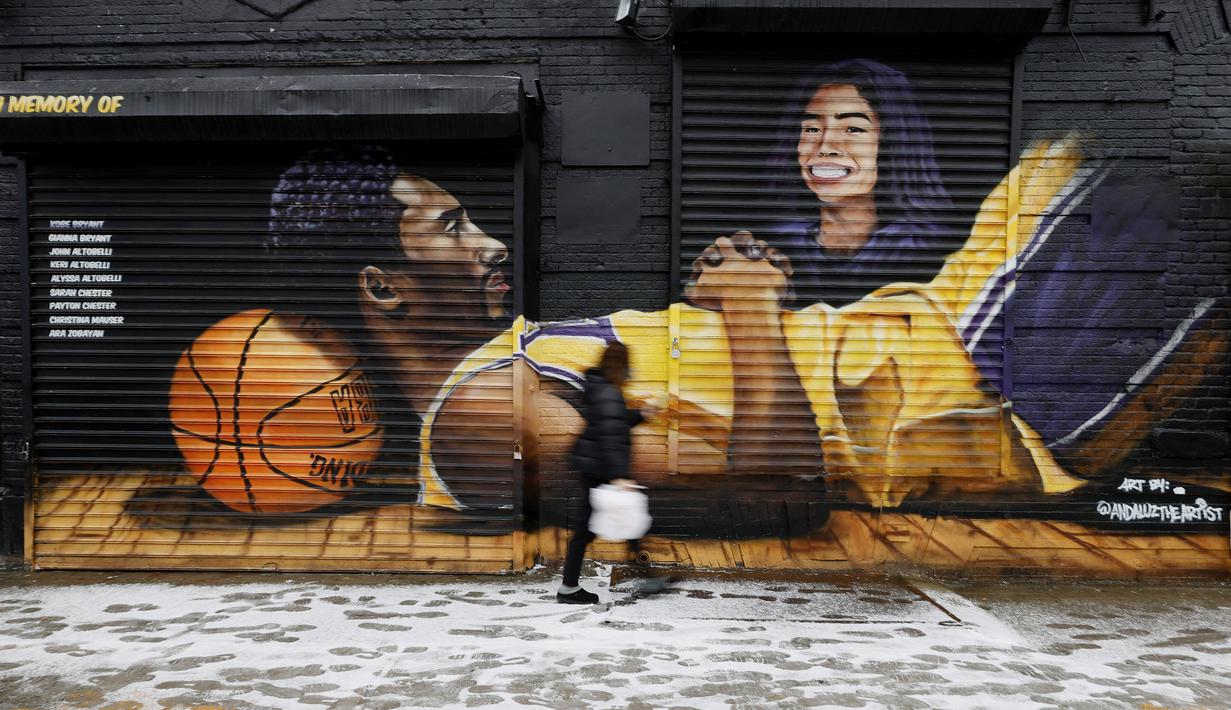 Seorang warga melintas di depan lukisan mural bintang LA Lakers, Kobe Bryant dan putrinya, Gianna di New York City, Selasa (26/1/2021). Lukisan dibuat untuk mengenang 1 tahun tragedi kecelakaan helikopter yang menewaskan keduanya. (Getty Images via AFP/Sarah Stier)