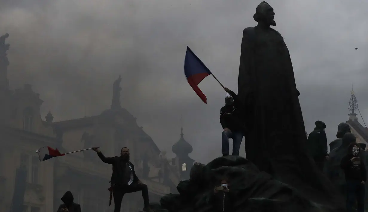 Demonstran memanjat monumen saat berkumpul untuk memprotes tindakan pembatasan COVID-19 di Old Town Square di Praha, Republik Ceko pada 18 Oktober 2020. Ceko  memberlakukan serangkaian tindakan pembatasan baru sebagai tanggapan atas rekor lonjakan infeksi virus corona. (AP Photo/Petr David Josek)