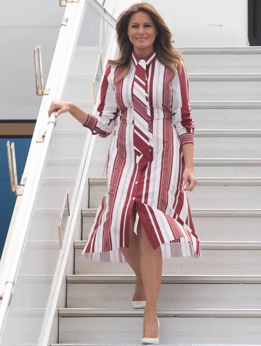 Ibu Negara AS, Melania Trump turun dari pesawat setibanya di Bandara Kotoka di Accra, Ghana, Selasa (2/10). Melania tampil modis dalam balutan shirt dress Celine dengan motif bergaris warna merah anggur, seharga sekitar Rp 30 juta. (AFP/SAUL LOEB)
