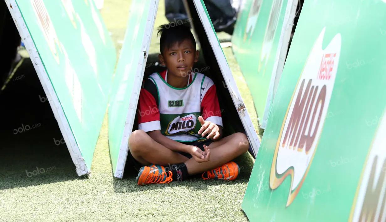 Seorang anak berteduh saat mengikuti Milo Football Clinic di Lapangan Sepak Bola Pertamina, Simprug, Jakarta, Minggu (24/4/2016). (Bola.com/Nicklas Hanoatubun)