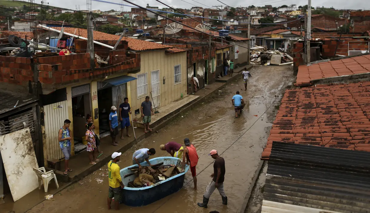 Warga membersihkan rumah mereka yang terendam banjir di Itapetinga, negara bagian Bahia, Brasil, Selasa (28/12/2021). Dua bendungan jebol pada Minggu (26/12) di timur laut Brasil, mengancam banjir yang lebih parah di wilayah yang diguyur hujan. (AP/Raphael Muller)