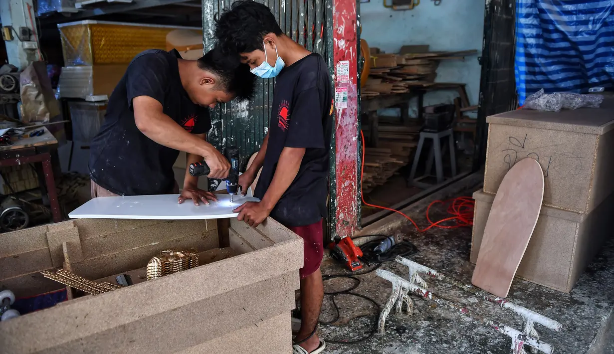 Pekerja toko peti mati Burapha mengebor lubang untuk membuat skateboard, terbuat dari kayu yang digunakan untuk peti mati, di Bangkok, 19 Maret 2021. Pembuat peti mati di Thailand mengubah kayu peti mati sisa menjadi skateboard murah di tengah booming popularitas olahraga. (Lillian SUWANRUMPHA/AFP)