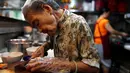 Nenek Leong Yuet Meng memotong daging babi di warungnya di Singapura (22/3). Nenek Leong turun langsung dengan dibantu beberapa asistennya untuk membuat mie pangsit dan menyajikannya di atas mangkuk. (Reuters/Edgar Su)