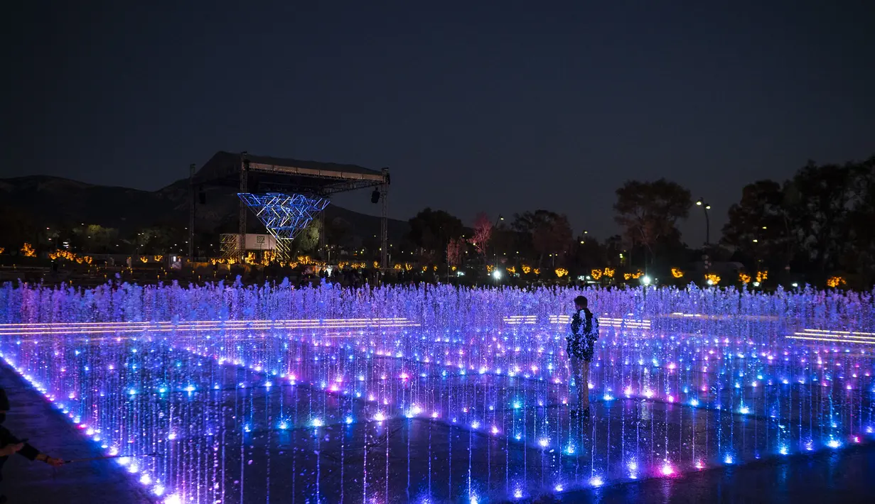 Seorang pria berdiri di dalam pertunjukan cahaya dan air Natal yang ditampilkan di Experience Park, di distrik pesisir Hellenikon di Athena, Yunani, Senin (20/12/2021).  (AFP/Angelos Tzortzinis)