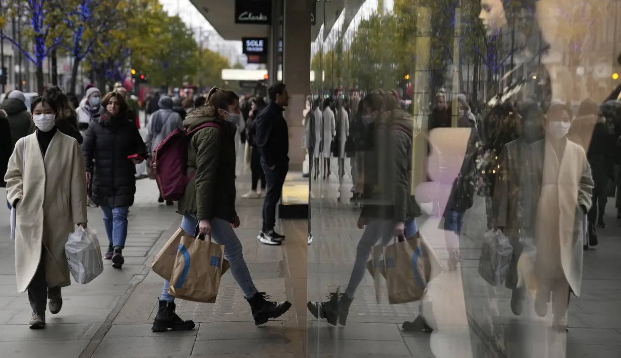 Seorang wanita tercermin saat berjalan ke sebuah toko di Oxford Street di London, Senin (29/11/2021). Di Inggris, kewajiban mengenakan masker akan berlaku lagi di toko-toko dan transportasi umum mulai Selasa menyusul temuan Covid-19 varian Omicron. (AP Photo/Matt Dunham)
