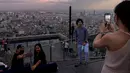 Orang-orang berfoto dari dek observasi di gedung pencakar langit King Power Mahanakhon saat matahari terbenam di Bangkok, Thailand pada 25 Oktober 2021. Gedung yang dibuka pada tahun 2017 lalu ini memiliki 77 lantai dengan tinggi 324 meter. (Jack TAYLOR / AFP)