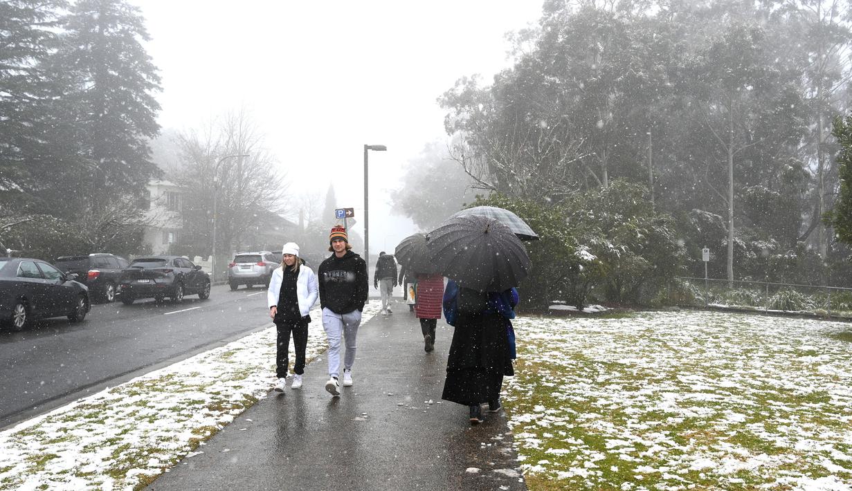 Orang-orang berjalan di sepanjang jalan selama hujan salju pertama musim ini di Katoomba di pegunungan Blue Mountains (10/6/2021). Suasana udara yang sejuk dan bersalju di Blue Mountains ketika musim dingin menjadi daya tarik wisatawan lokal di Sydney. (AFP/Saeed KHAN)