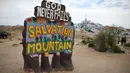 Sebuah tanda yang menandai pintu masuk ke Salvation Mountain, sebuah lereng bukti di Niland, California, Amerika Serikat. Dibuat oleh penduduk lokal bernama Leonard Knight, Salvation diisi dengan banyak seni lukis berupa mural dengan kutipan Kristen dan ayat-ayat Alkitab. (Robyn Beck/AFP)