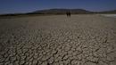Penjaga kota berjalan di dasar laguna Alalay yang kering dan retak di Cochabamba, Bolivia, Jumat (18/11/2022). Dua laguna, Coña Coña dan Alalay, berada pada level kritis karena kurangnya hujan, penumpukan bahan organik dan penguapan di tengah peningkatan suhu. (AP Photo/Juan Karita)