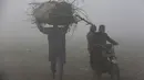 Seorang pria dan pengendara sepeda motor melintasi lapangan saat kabut tebal mengurangi jarak pandang di Lahore, Pakistan, Selasa (30/11/2021). Lahore secara konsisten menempati peringkat sebagai salah satu kota terburuk di dunia untuk polusi udara. (AP Photo/K.M. Chaudary)