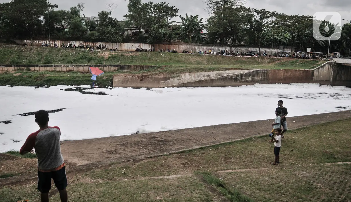 Warga bermain di pinggir aliran Kanal Banjir Timur (KBT), Duren Sawit, Jakarta, Kamis (2/7/2020). Penampakan busa yang memenuhi aliran KBT akibat limbah pabrik dan rumah tangga sejak dua minggu lalu itu menjadi tontonan warga meski menimbulkan bau tak sedap. (merdeka.com/Iqbal Nugroho)