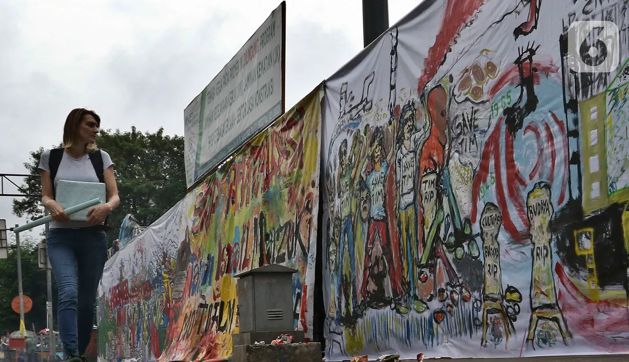 Warga berjalan di samping proyek revitalisasi Taman Ismail Marzuki (TIM) yang dipenuhi lukisan bentuk protes, Jakarta, Sabtu (29/2/2020). Kebijakan Pemprov DKI Jakarta merevitalisasi TIM dinilai cacat prosedural karena tidak pernah dibicarakan dengan seniman sebelumnya. (Liputan6.com/Johan Tallo)