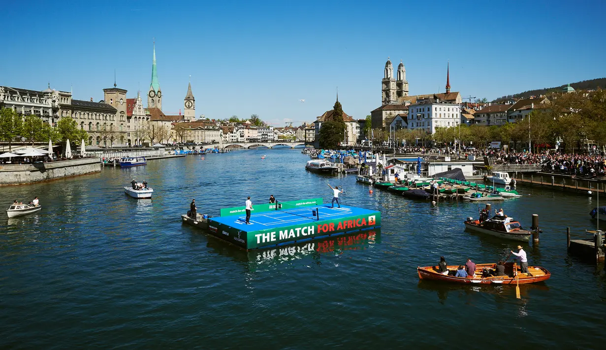 Petenis asal Swiss, Roger Federer (kiri) bertanding melawan petenis asal Inggris, Andy Murray di lapangan kecil di atas sungai Kota Zurich, Senin (10/4). Kedua petenis itu terlibat dalam program amal The Match For Africa 3. (Michael Buholzer/AFP)