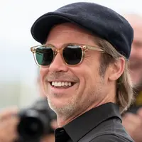 Aktor Brad Pitt tersenyum saat tiba menghadiri pemutaran film 'Once Upon a Time in Hollywood' selama Festival Film Cannes Internasional ke-72 di Prancis (22/5/2019).  Brad Pitt tampil santai mengenakan jeans hitam, kemeja polo hitam, kaca mata dan topi. (AP Photo/Joel C Ryan)