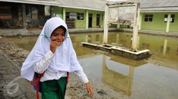 Siswa MI Mansyaul Huda melewati pelataran sekolah yang terkena dampak abrasi pantai Muara Gembong, Bekasi, Selasa, (26/7). Tingkat abrasi yang tinggi menyebabkan sejumlah rumah terkikis dan beberapa sekolah terendam air laut. (Liputan6.com/Gempur M Surya)