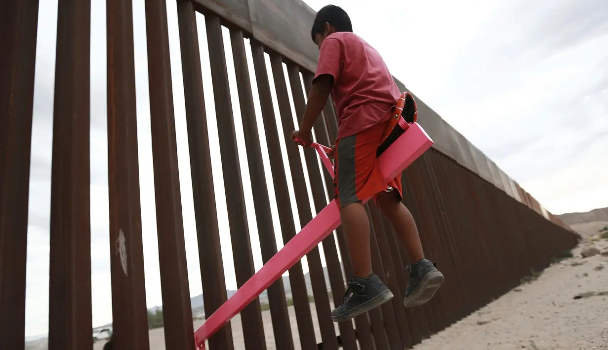 Seorang anak bermain jungkat-jungkit yang dipasang di antara pagar pemisah Meksiko dengan Amerika Serikat, Ciudad de Juarez, Meksiko, Minggu (28/7/2019). Jungkat-jungkit tersebut dirancang seorang profesor arsitektur California, Ronald Rael. (AP Photo/Christian Chavez)