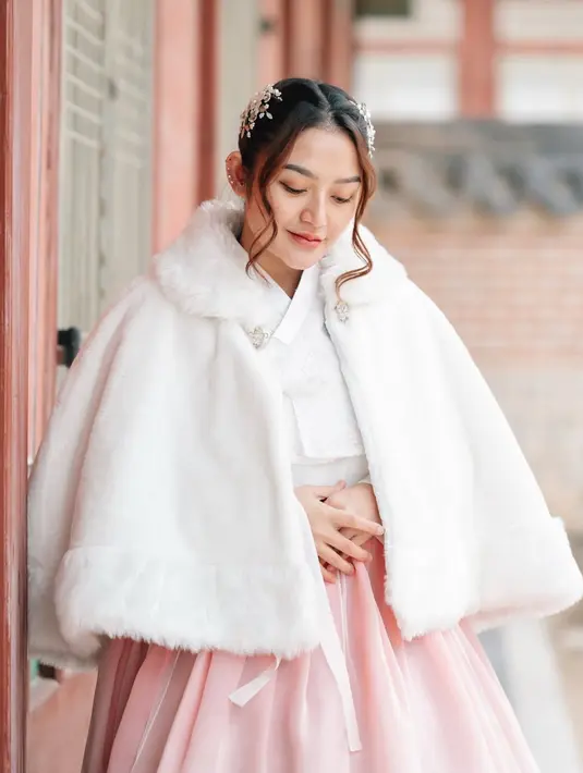 Siti Badriah tampak mengenakan hanbok warna putih untuk atasan dan rok soft pink. Lengkap dengan mantel putih kerah berbulu. [@sitibadriahh]