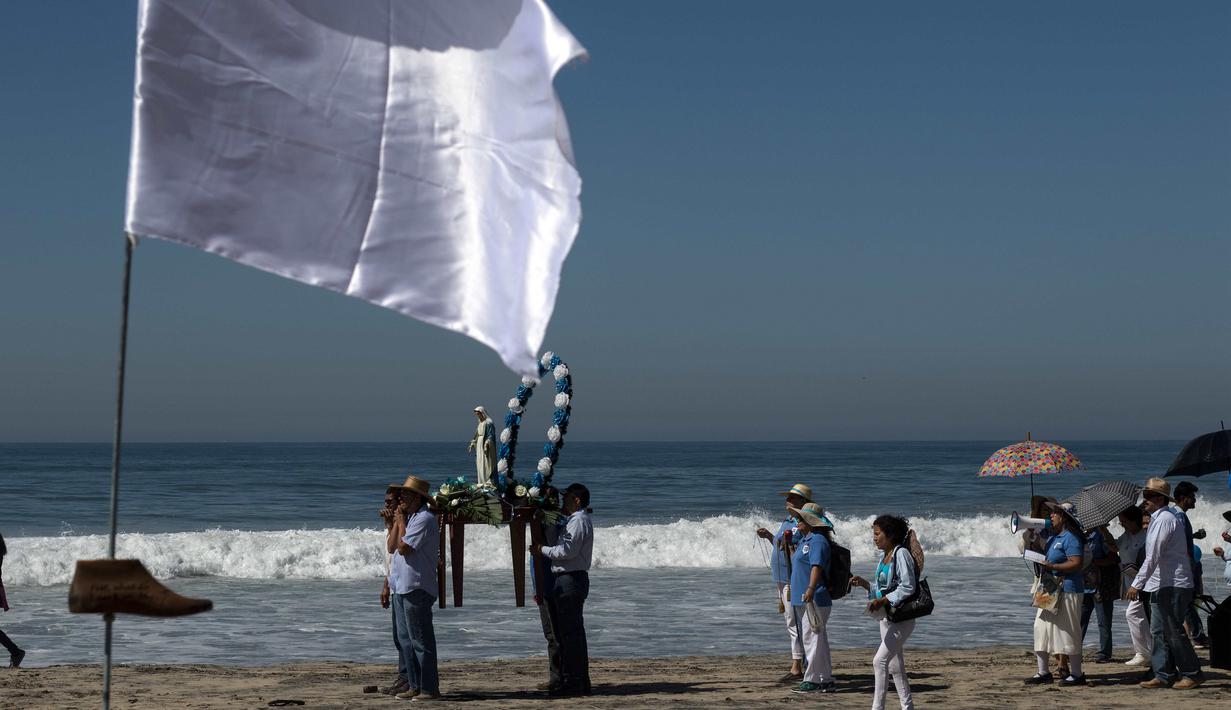 Warga setempat melakukan prosesi keagamaan dekat seni instalasi kontemporer "Tu huella es el camino, tu bandera es de paz" di Playas de Tijuana, Meksiko (7/10). (AFP Photo/Guillermo Arias)