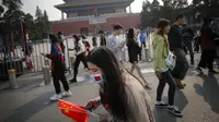 Seorang wanita mengenakan masker untuk mencegah penyebaran virus corona memegang bendera nasional Kota Terlarang selama Hari Nasional di Beijing, Rabu, (7/10/2020). Turis Tiongkok melakukan 425 juta perjalanan domestik pada paruh pertama dari delapan hari libur Hari Nasional. (AP Photo/Andy Wong)