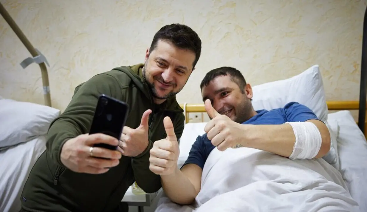 Dalam foto yang disediakan oleh Kantor Pers Kepresidenan Ukraina pada 13 Maret 2022, Presiden Ukraina Volodymyr Zelenskyy (kiri) berfoto dengan seorang tentara yang terluka saat kunjungannya ke sebuah rumah sakit di Kiev, Ukraina. (Ukrainian Presidential Press Office via AP)