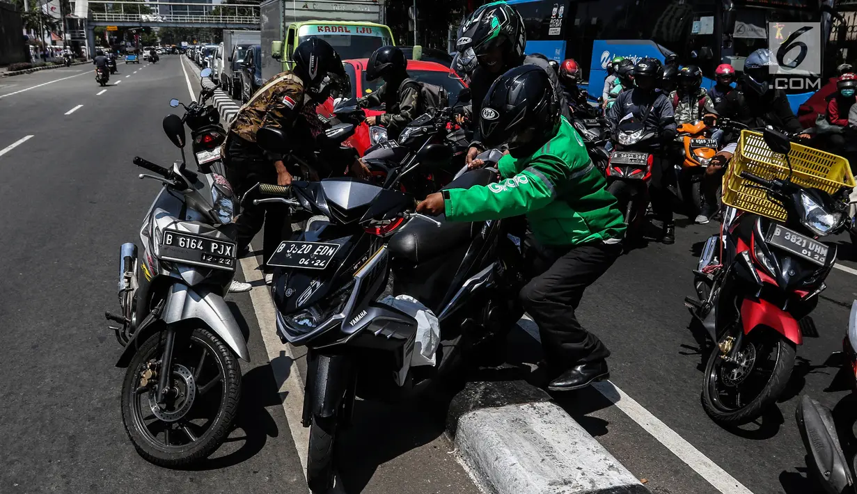 Sejumlah pengendara bergotong royong mengangkat sepeda motor mereka melewati pembatas jalan untuk berpindah jalur di kawasan Ridwan Rais, Jakarta, Rabu (21/8/2019). Pengendara motor tersebut berpindah jalur disebabkan tidak sabar menunggu kemacetan. (Liputan6.com/Johan Tallo)