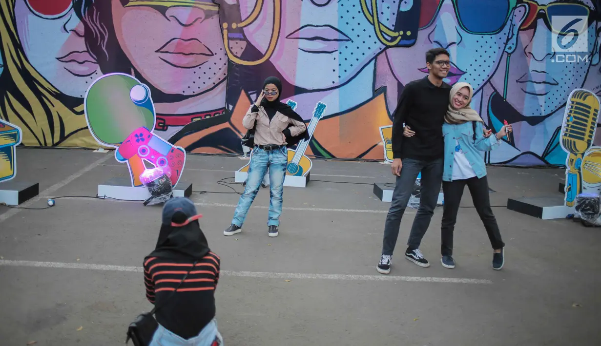 Pengunjung berfoto dengan latar belakang mural saat menghadiri acara Playfest 2019 di Parkir Selatan Gelora Bung Karno, Jakarta, Minggu (25/8/2019). Playfest memasuki tahun kedua yang digelar oleh Narasi TV. (Liputan6.com/Faizal Fanani)