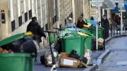 Orang-orang berjalan melewati tong sampah dan tumpukan kantong sampah yang menumpuk di Paris (4/2/2020). Sampah menumpuk di jalan-jalan Paris dan Marseille karena pemogokan perubahan pada sistem pensiun nasional Prancis.  (AP Photo/Christophe Ena)